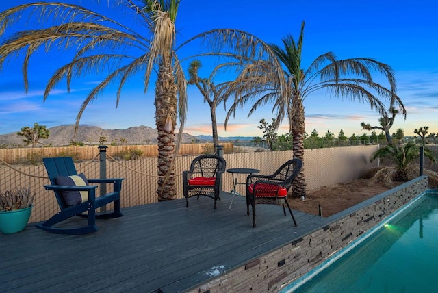 deck at dusk featuring a fenced in pool and a mountain view