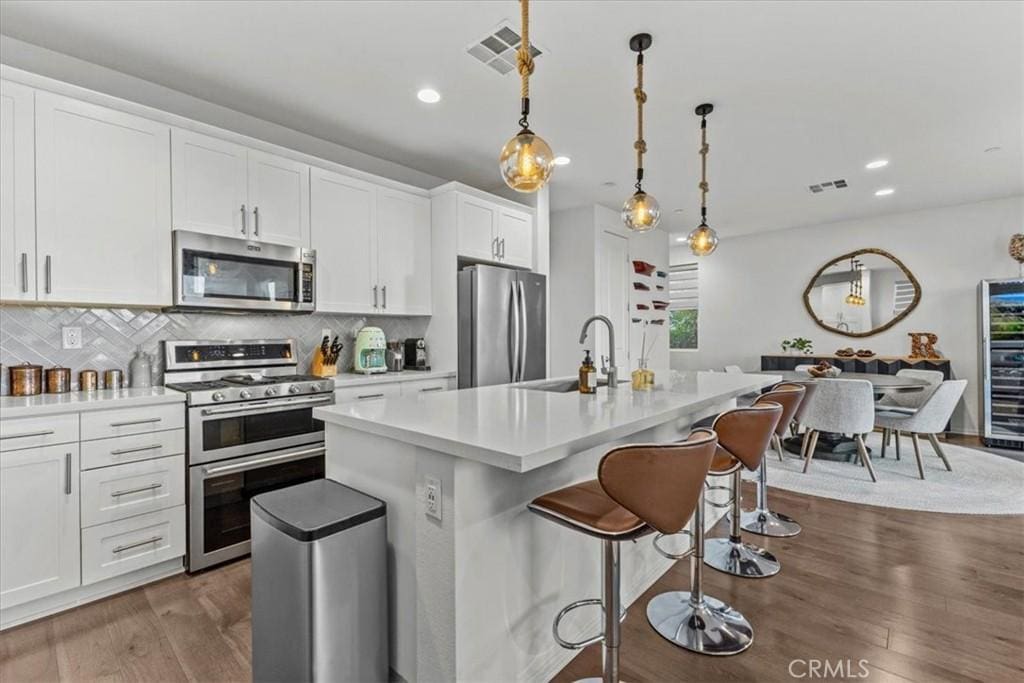 kitchen featuring a center island with sink, hanging light fixtures, appliances with stainless steel finishes, and tasteful backsplash