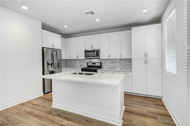 kitchen with sink, appliances with stainless steel finishes, white cabinets, and light hardwood / wood-style floors