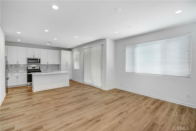 kitchen featuring decorative backsplash, appliances with stainless steel finishes, white cabinetry, a kitchen island with sink, and light hardwood / wood-style floors