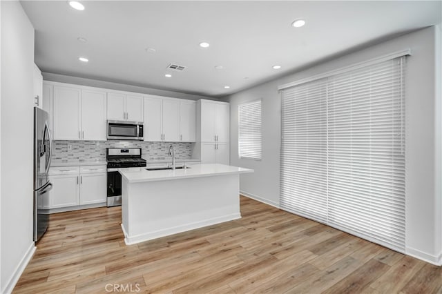 kitchen featuring appliances with stainless steel finishes, sink, light wood-type flooring, white cabinetry, and a center island with sink