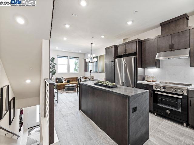 kitchen featuring electric stove, hanging light fixtures, a kitchen island, dark brown cabinetry, and stainless steel refrigerator