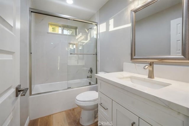 full bathroom featuring vanity, hardwood / wood-style flooring, toilet, and bath / shower combo with glass door