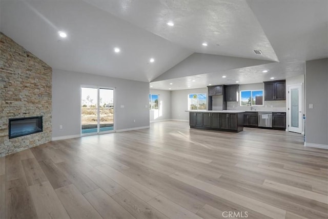 unfurnished living room with a stone fireplace, light wood-type flooring, and high vaulted ceiling