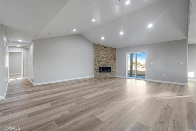 unfurnished living room featuring lofted ceiling, a stone fireplace, and light wood-type flooring