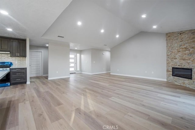 unfurnished living room with a stone fireplace, light hardwood / wood-style floors, and vaulted ceiling