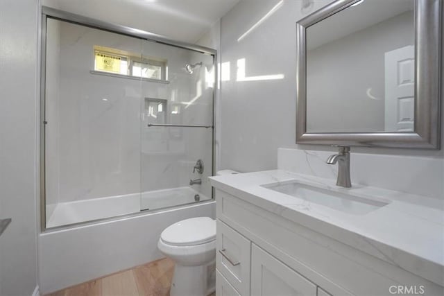 full bathroom featuring hardwood / wood-style floors, vanity, toilet, and bath / shower combo with glass door