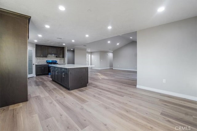 kitchen with dark brown cabinets, a kitchen island, decorative backsplash, and light hardwood / wood-style flooring