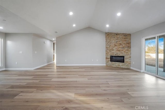 unfurnished living room with light wood-type flooring, vaulted ceiling, and a stone fireplace