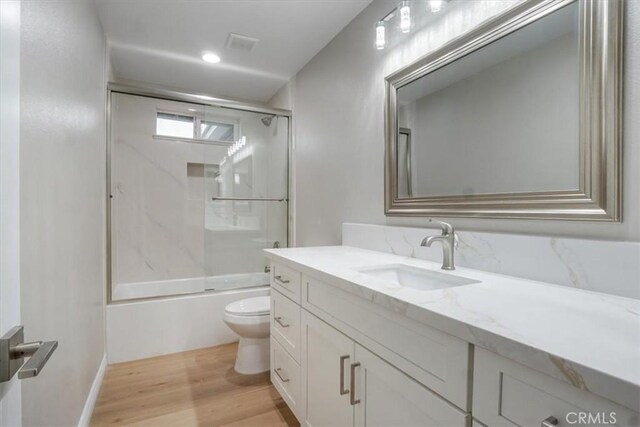 full bathroom with hardwood / wood-style floors, vanity, toilet, and combined bath / shower with glass door