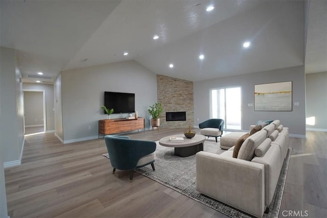 living room featuring a stone fireplace, high vaulted ceiling, and light hardwood / wood-style flooring