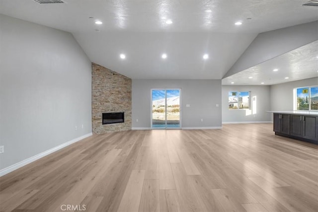 unfurnished living room featuring a stone fireplace, a wealth of natural light, and light hardwood / wood-style flooring