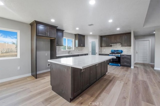 kitchen featuring gas stove, dark brown cabinets, a kitchen island, and light hardwood / wood-style floors