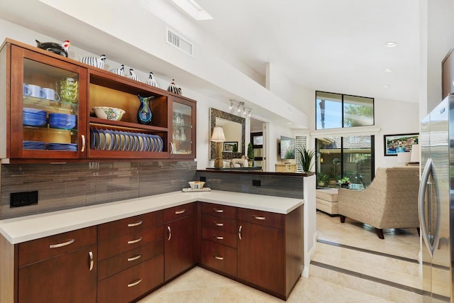 kitchen with kitchen peninsula, light tile patterned floors, backsplash, and stainless steel refrigerator