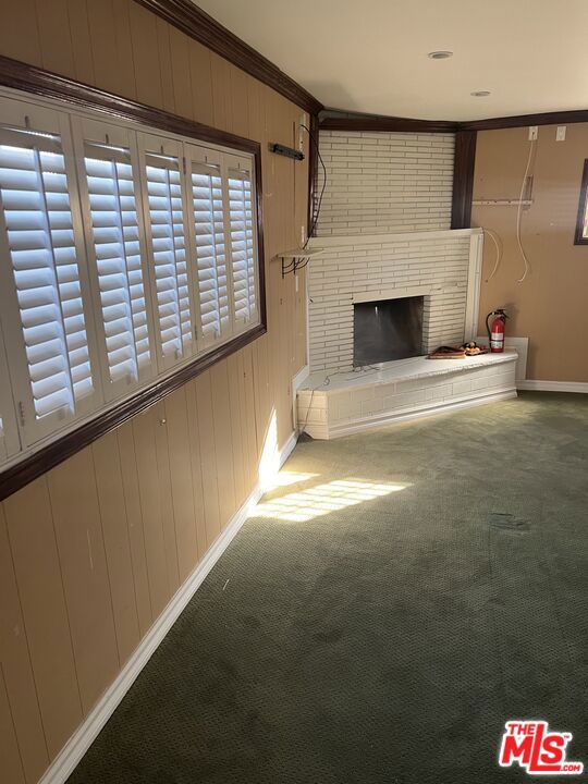 unfurnished living room featuring crown molding, a fireplace, carpet floors, and wood walls