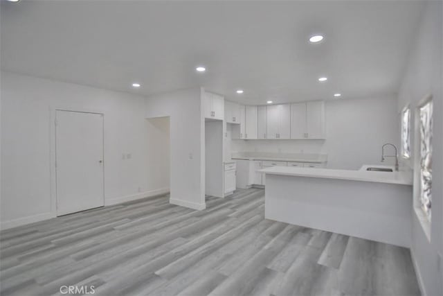 kitchen with kitchen peninsula, sink, white cabinets, and light hardwood / wood-style floors