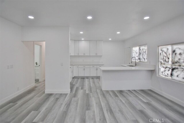 kitchen with white cabinets, kitchen peninsula, sink, and light hardwood / wood-style flooring