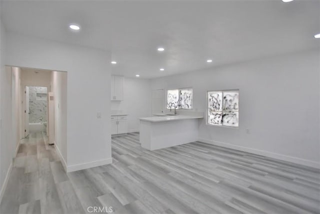 interior space featuring kitchen peninsula, white cabinets, light hardwood / wood-style flooring, and sink