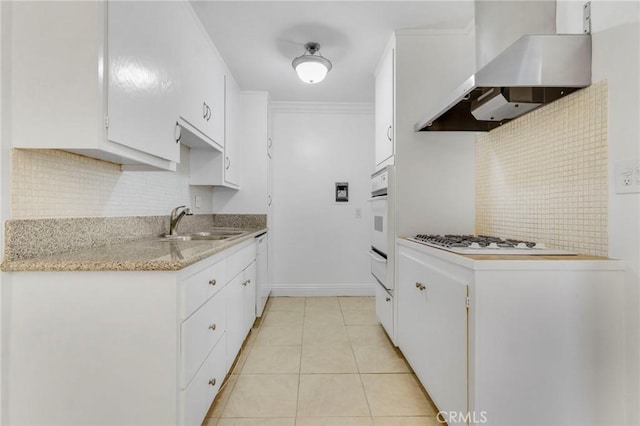 kitchen with white appliances, wall chimney range hood, sink, ornamental molding, and white cabinetry