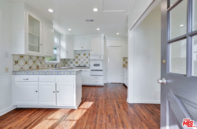 kitchen featuring white oven, tasteful backsplash, white cabinetry, and dark wood-type flooring