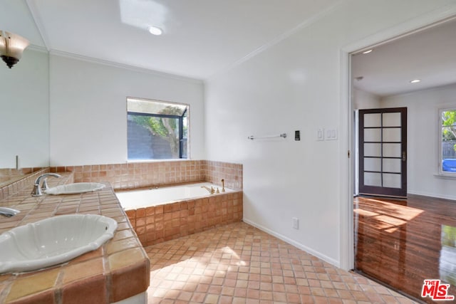 bathroom with crown molding, sink, and a relaxing tiled tub