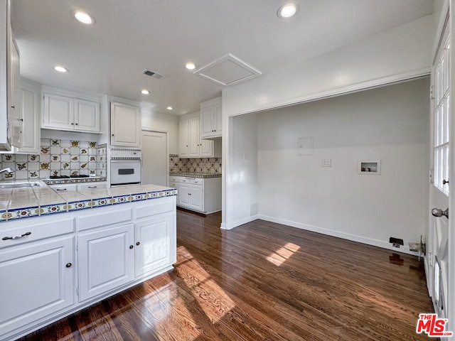 kitchen with decorative backsplash, dark hardwood / wood-style flooring, white cabinetry, and white oven