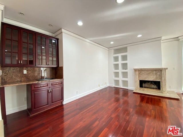 unfurnished living room featuring dark hardwood / wood-style floors, sink, ornamental molding, and a premium fireplace