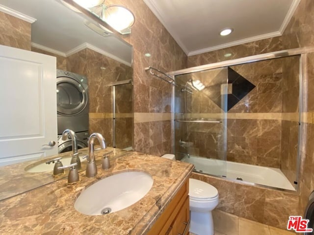 full bathroom featuring vanity, stacked washer and dryer, tile walls, toilet, and combined bath / shower with glass door