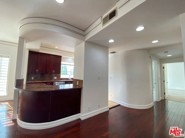 kitchen with kitchen peninsula, ornamental molding, backsplash, and hardwood / wood-style flooring