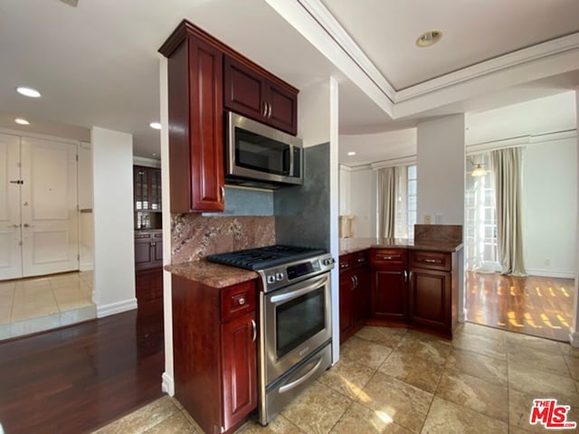 kitchen with appliances with stainless steel finishes, dark stone counters, backsplash, kitchen peninsula, and crown molding