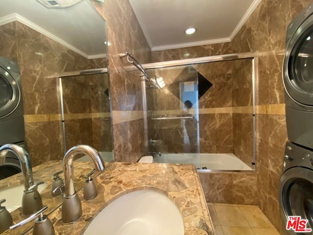 bathroom with stacked washer / dryer, sink, tile walls, combined bath / shower with glass door, and crown molding