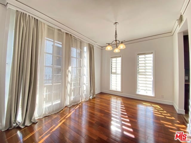 unfurnished dining area featuring dark hardwood / wood-style floors, ornamental molding, and an inviting chandelier