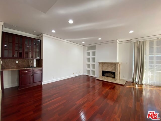 unfurnished living room featuring dark wood-type flooring, a premium fireplace, and crown molding