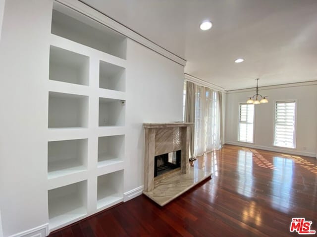 unfurnished living room featuring dark wood-type flooring, a high end fireplace, built in features, and a notable chandelier