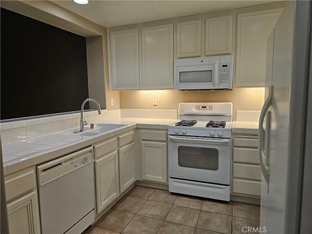 kitchen with tile countertops, white appliances, sink, light tile patterned flooring, and white cabinetry