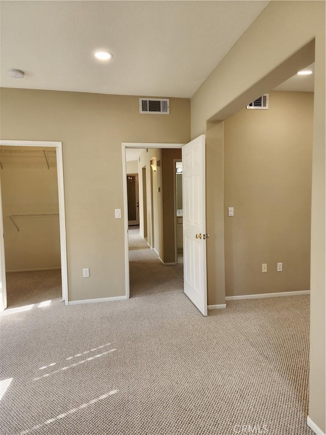 unfurnished bedroom with light colored carpet, a walk in closet, and a closet