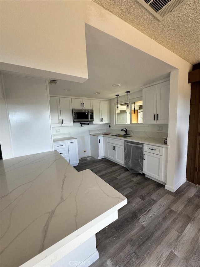 kitchen with light stone countertops, appliances with stainless steel finishes, white cabinetry, sink, and pendant lighting