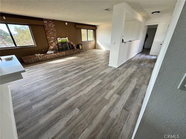 unfurnished living room featuring a fireplace, wood-type flooring, a textured ceiling, and wooden walls