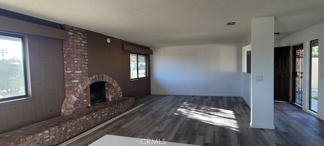 unfurnished living room featuring a brick fireplace, a textured ceiling, dark hardwood / wood-style floors, and wood walls