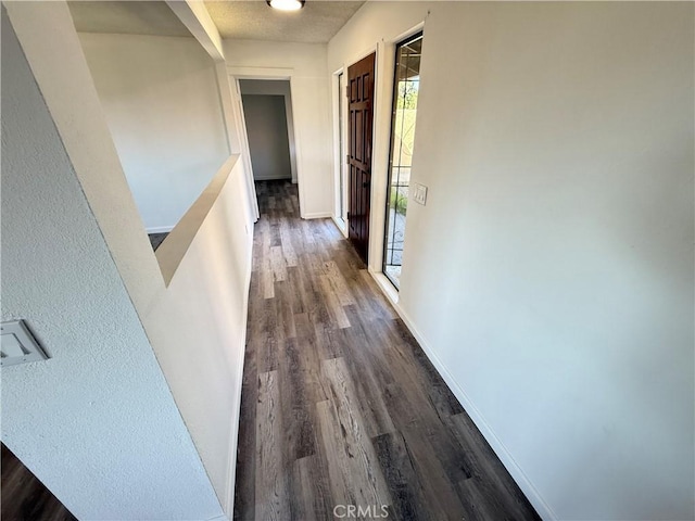 corridor with an upstairs landing, baseboards, and dark wood finished floors