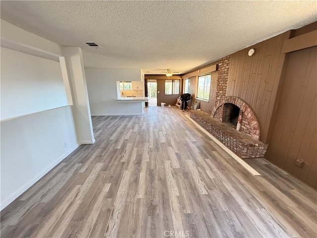 unfurnished living room featuring visible vents, a textured ceiling, wood finished floors, wood walls, and a brick fireplace
