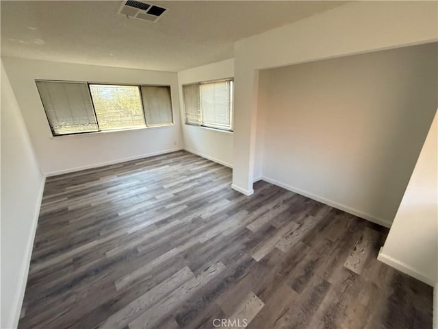 empty room with dark wood-style floors, visible vents, and baseboards