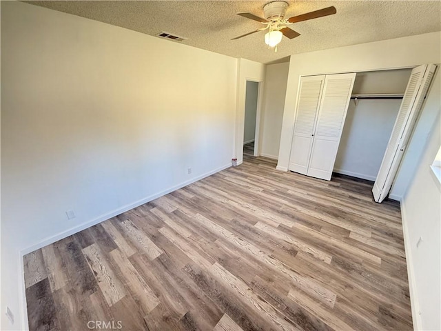 unfurnished bedroom with wood finished floors, baseboards, visible vents, a closet, and a textured ceiling