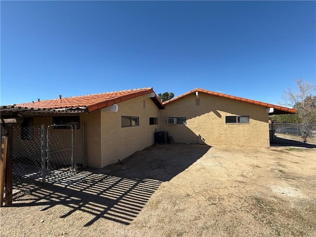 back of house featuring stucco siding, a tiled roof, fence, and a gate