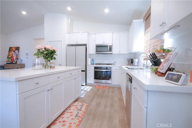 kitchen featuring appliances with stainless steel finishes, sink, light hardwood / wood-style flooring, white cabinetry, and lofted ceiling