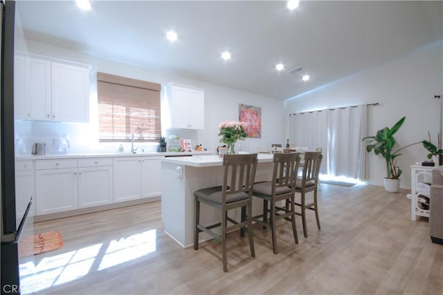 kitchen with white cabinets, light wood-type flooring, and an island with sink