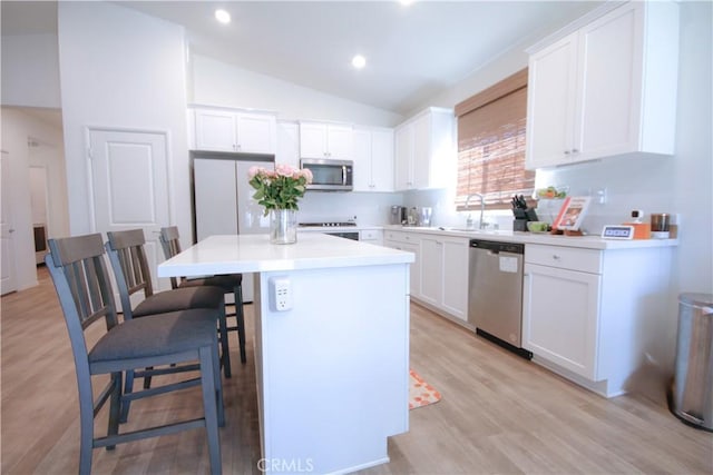 kitchen with stainless steel appliances, vaulted ceiling, a kitchen island, sink, and white cabinetry