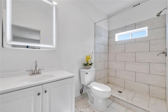 bathroom with a tile shower, vanity, and toilet