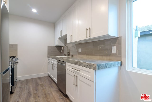 kitchen featuring white cabinetry, sink, stainless steel appliances, decorative backsplash, and light wood-type flooring