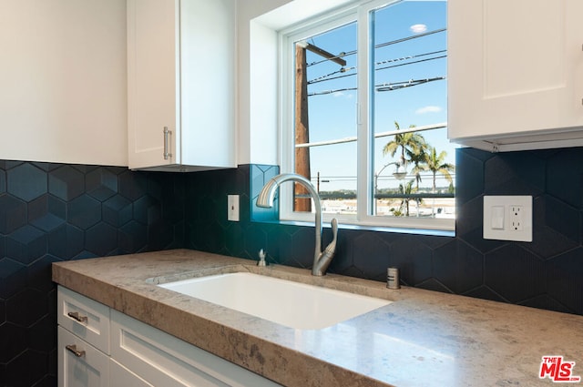 kitchen with light stone countertops, white cabinetry, and sink